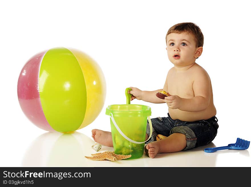 A shirtless baby boy in rolled up jeans with a beach ball and sandpail full of ocean shells. Isolated on white. A shirtless baby boy in rolled up jeans with a beach ball and sandpail full of ocean shells. Isolated on white.