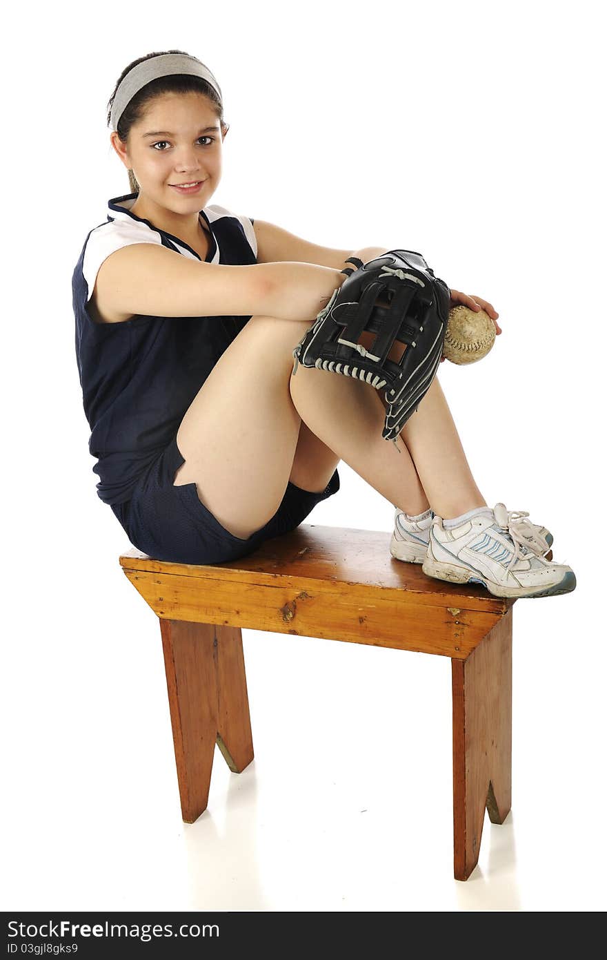 An attractive young teen happily sitting on an old bench wearing her team's softball uniform.  She holds a new mitt and a well worn ball. An attractive young teen happily sitting on an old bench wearing her team's softball uniform.  She holds a new mitt and a well worn ball.