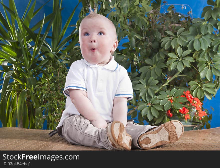 Baby sits on a background of green shrubs.