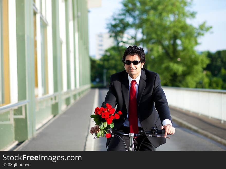 Businessman with suit is coming from work riding a bicycle with bouquet of red roses