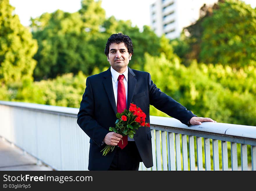 Businessman in a suit with bouquet of red roses standing on the bridge. Businessman in a suit with bouquet of red roses standing on the bridge