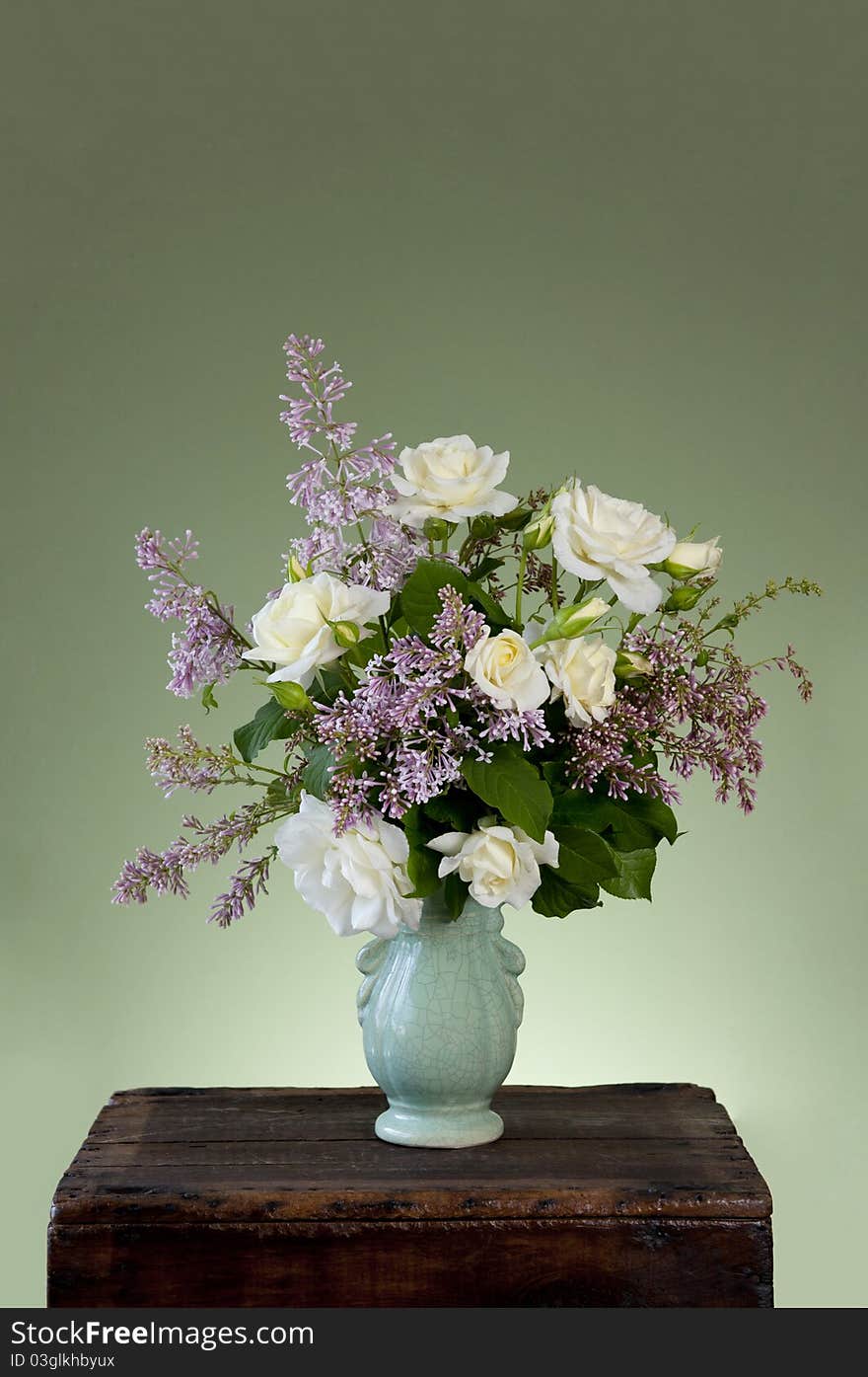 A spring flower arrangement with white roses and lilac in a antique vase with green background