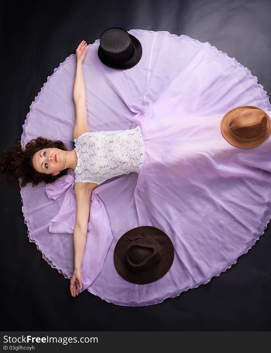 Attractive woman lying on the floor in liliac dress with a three hats