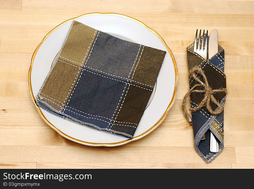 Knife and fork in textile napkin on wooden table