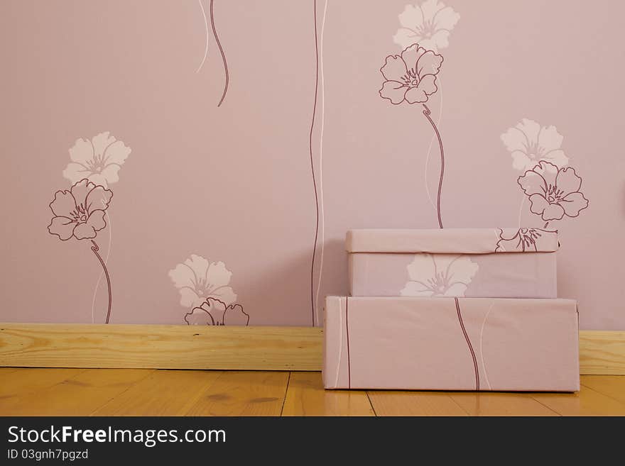 Purple wallpaper with flowers and a wooden floor in the room. On the floor there are two purple boxes. Purple wallpaper with flowers and a wooden floor in the room. On the floor there are two purple boxes