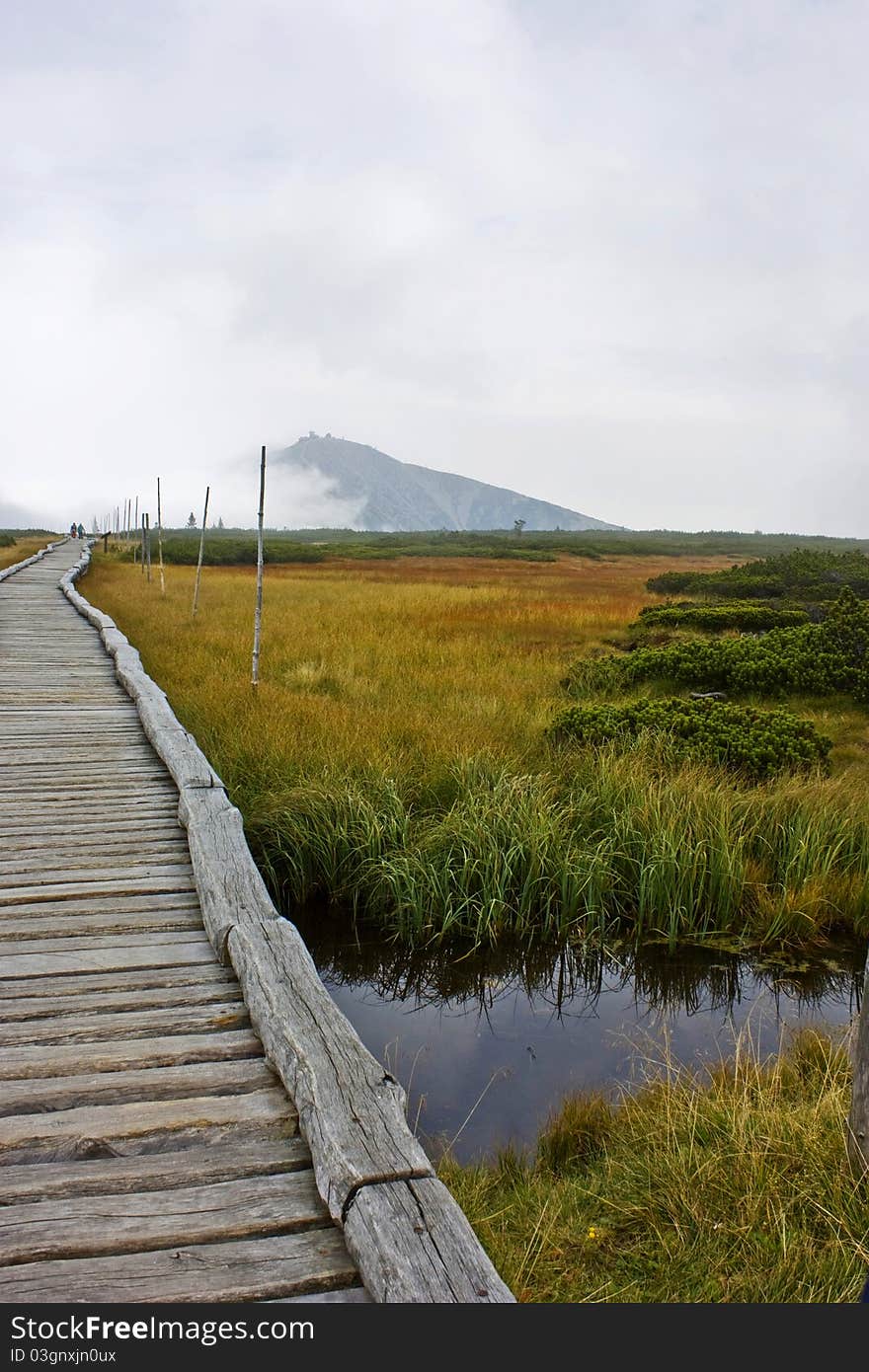 The wooden path to the Czech Republic's highest mountain surrounded by wetlands and fog. There are some tourists in the background. Shot in October. The wooden path to the Czech Republic's highest mountain surrounded by wetlands and fog. There are some tourists in the background. Shot in October.