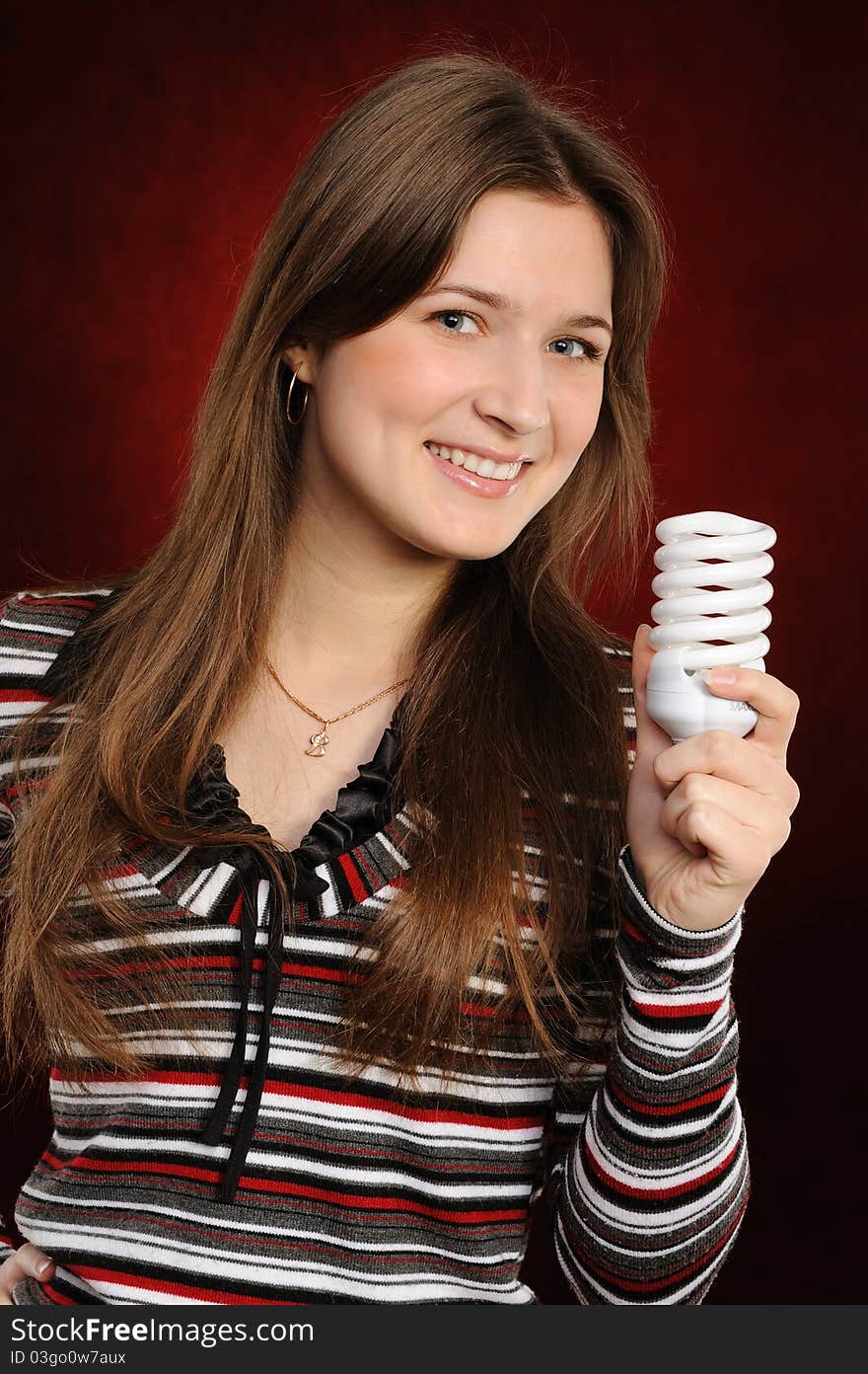 Young woman holding an fluorescent light bulb. On a red background