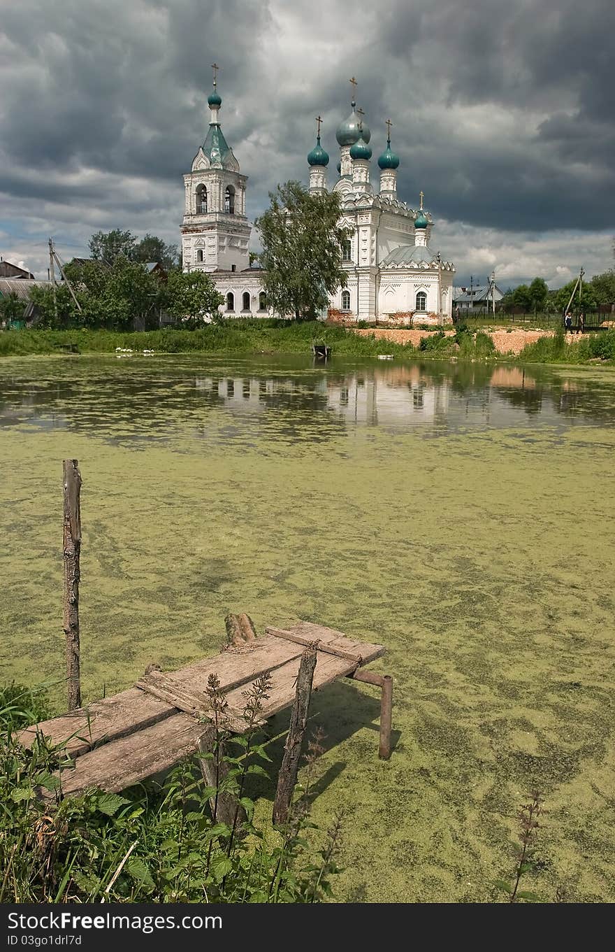 Christian temple at a pond in Dmitrovsky area of Moscow suburbs. The middle of summer. Rainy clouds are condensed over a temple. Cloudy weather. The rain will soon begin. Christian temple at a pond in Dmitrovsky area of Moscow suburbs. The middle of summer. Rainy clouds are condensed over a temple. Cloudy weather. The rain will soon begin.