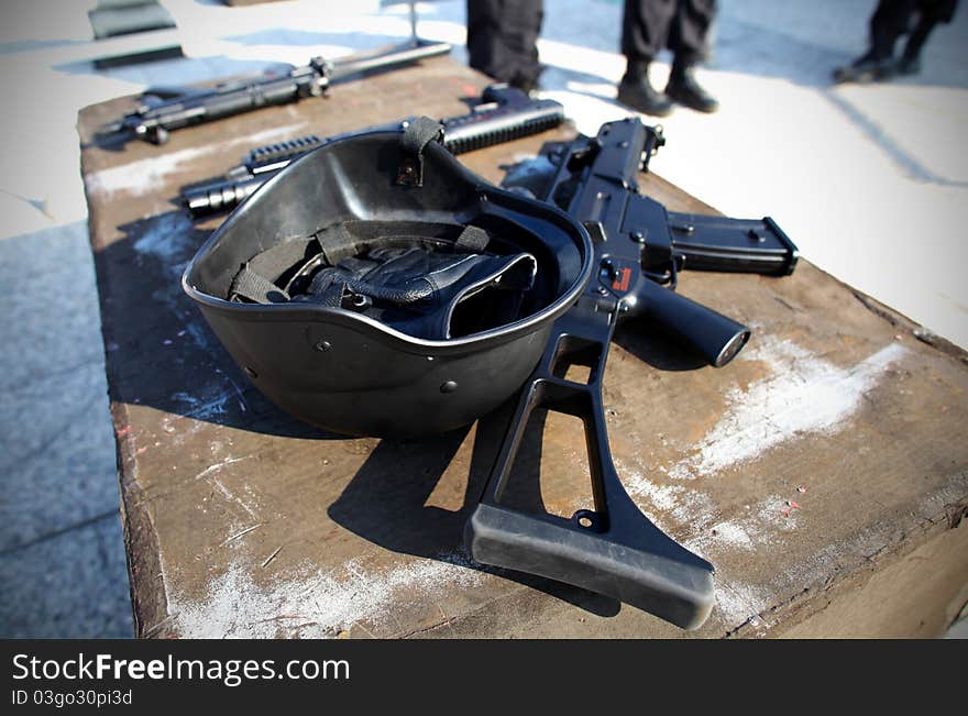 Helmet and a gun with police in the background.