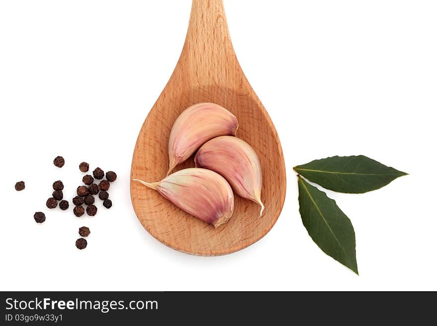 Garlic in a wooden spoon with bay leaf herb and black peppercorns isolated over white background. Garlic in a wooden spoon with bay leaf herb and black peppercorns isolated over white background.