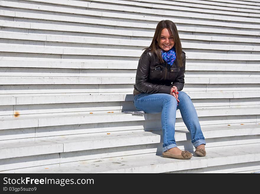 Attractive young woman sitting on the marble steps and smiles in the sunlight.