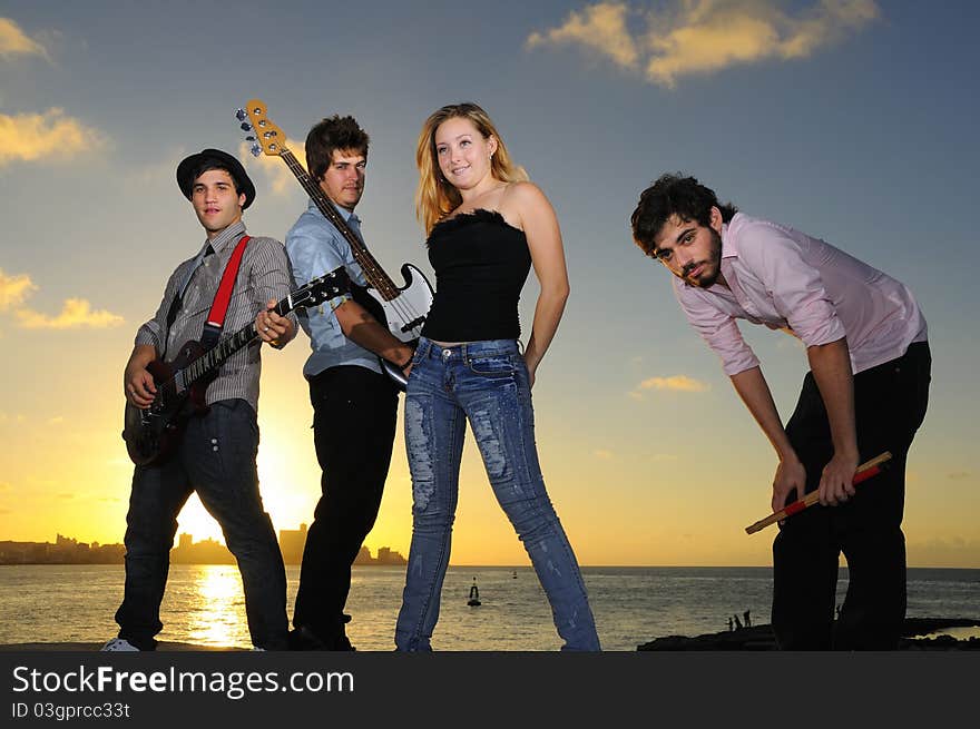 Portrait of young musical band with 3 boys and a girl posing outdoors at sunset with instruments. Portrait of young musical band with 3 boys and a girl posing outdoors at sunset with instruments