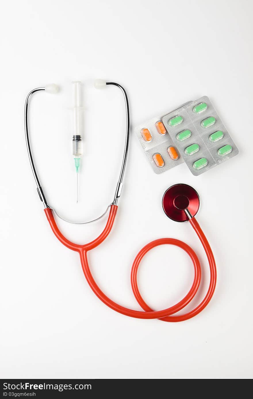 Single red shiny stethoscope with green and orange pills and a serynge on white background. Single red shiny stethoscope with green and orange pills and a serynge on white background