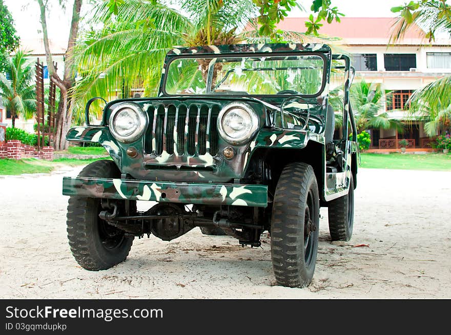 An all wheel drive camouflage painted jeep on a sandy ground and palm greenery background