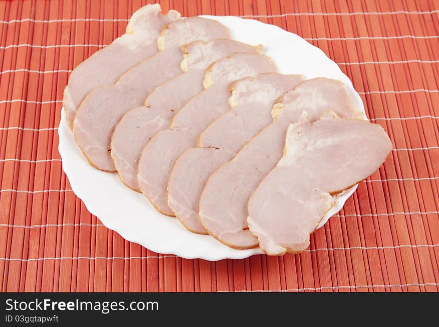 Smoked and sliced meat on the white plate standing on the red mat.