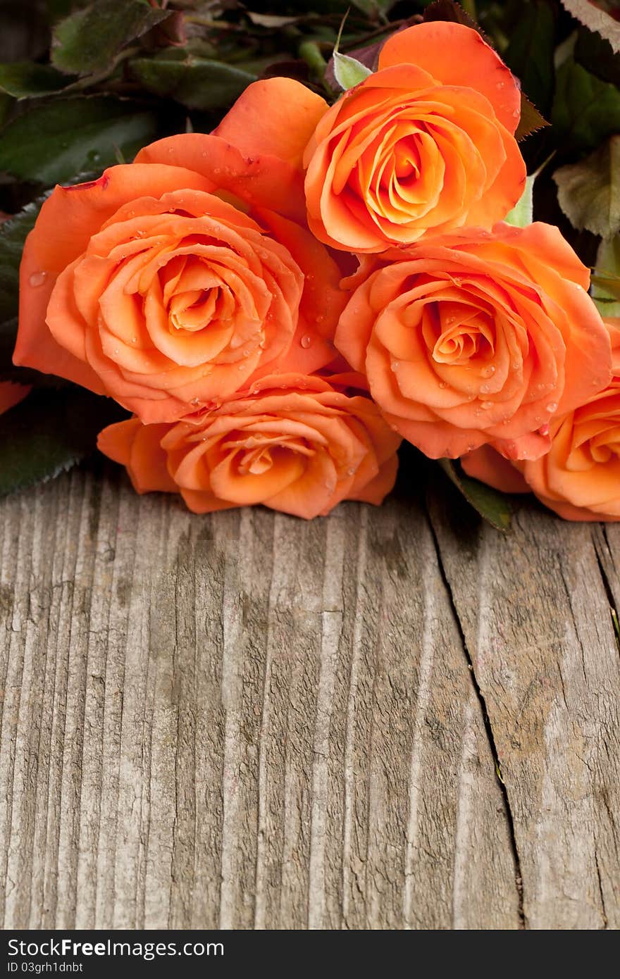 Bunch of orange roses on old wooden table as background