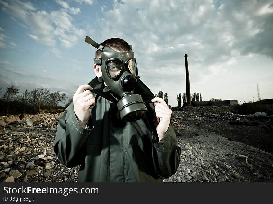 Bizarre portrait of man in gas mask on smoky industrial background with pipes after nuclear disaster