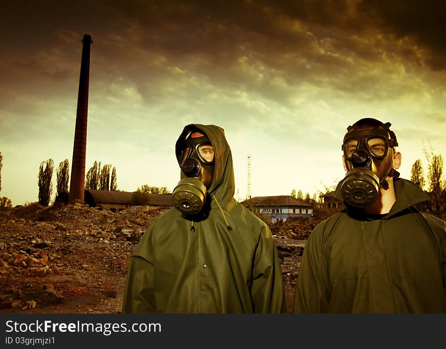 Two men in gas masks on smoky industrial background with pipes after nuclear disaster