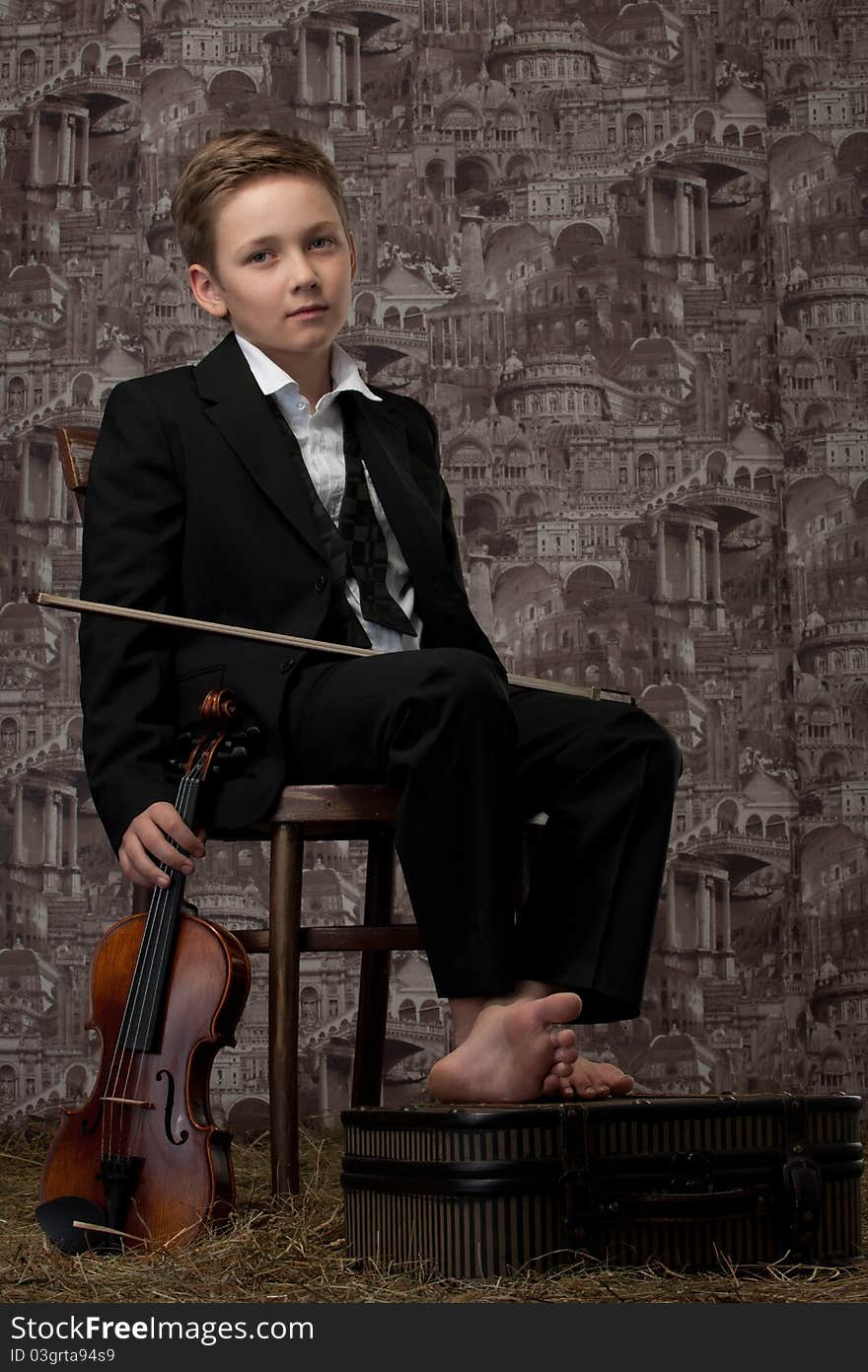 The tired boy in a classical suit sits on a chair with a violin in hands. The tired boy in a classical suit sits on a chair with a violin in hands