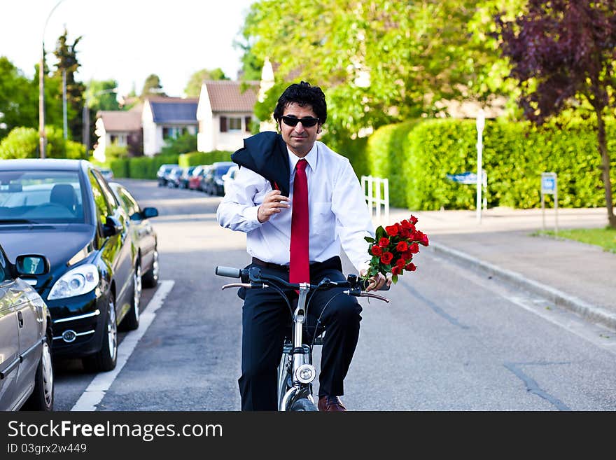 Businessman in a suit is riding a bicycle with bouquet of roses. Businessman in a suit is riding a bicycle with bouquet of roses