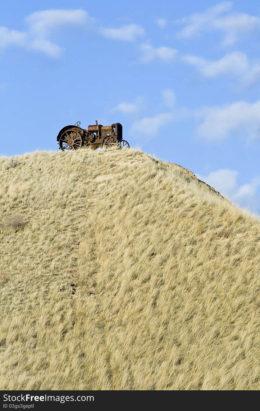 A rustic tractor sitting on the top of a grassy hill in Montana.