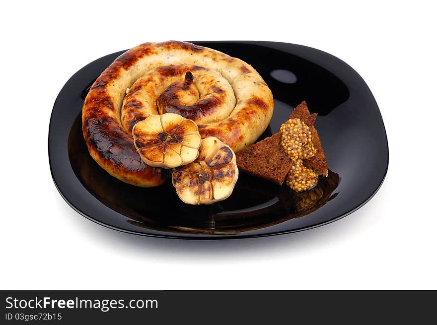 Sausage with toast, baked garlic and french mustard on black plate isolated on a white background.