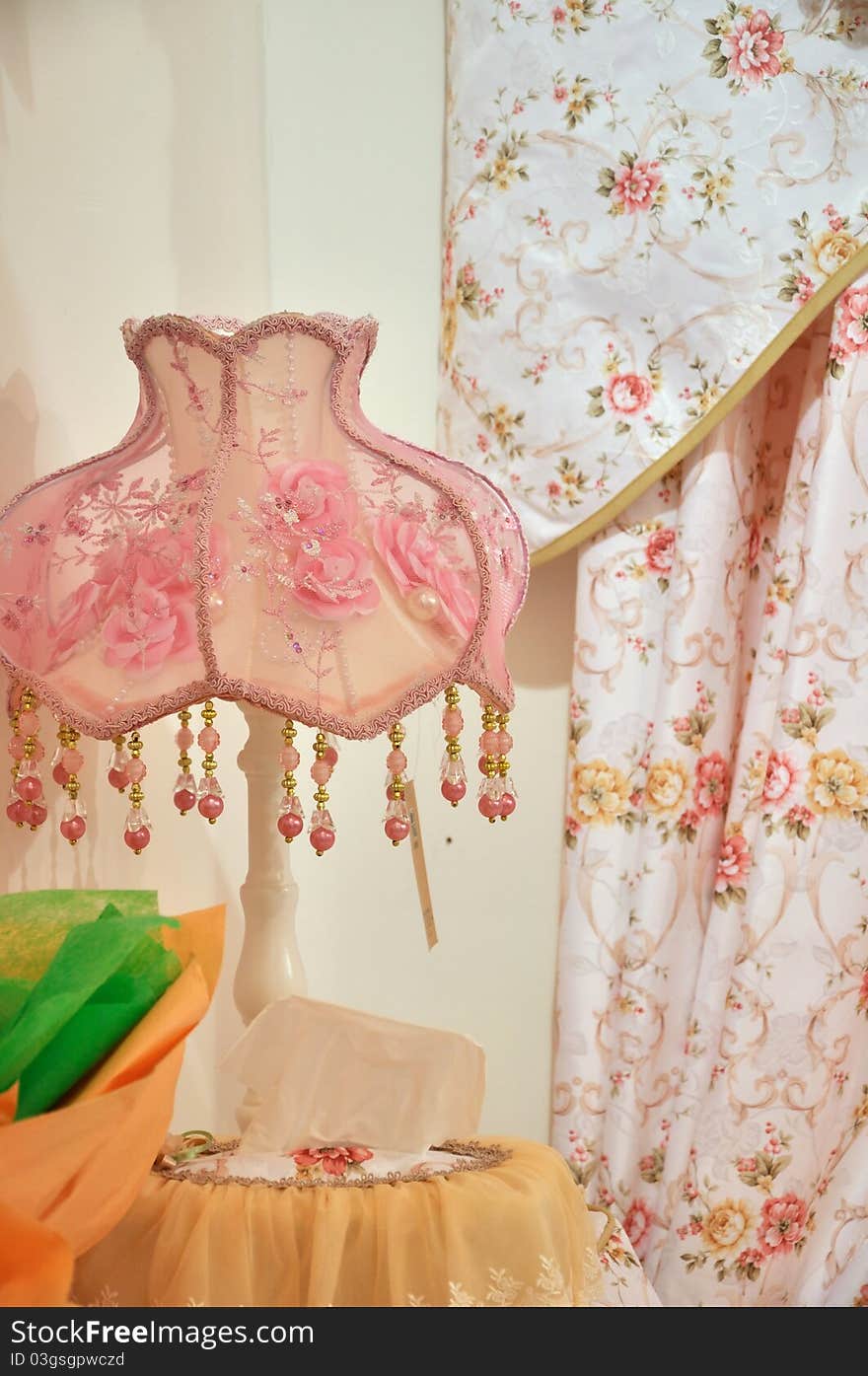 Lamp in pink color cover, beside flowery and light color curtain, shown as room for female interior detail and warm style. Lamp in pink color cover, beside flowery and light color curtain, shown as room for female interior detail and warm style.