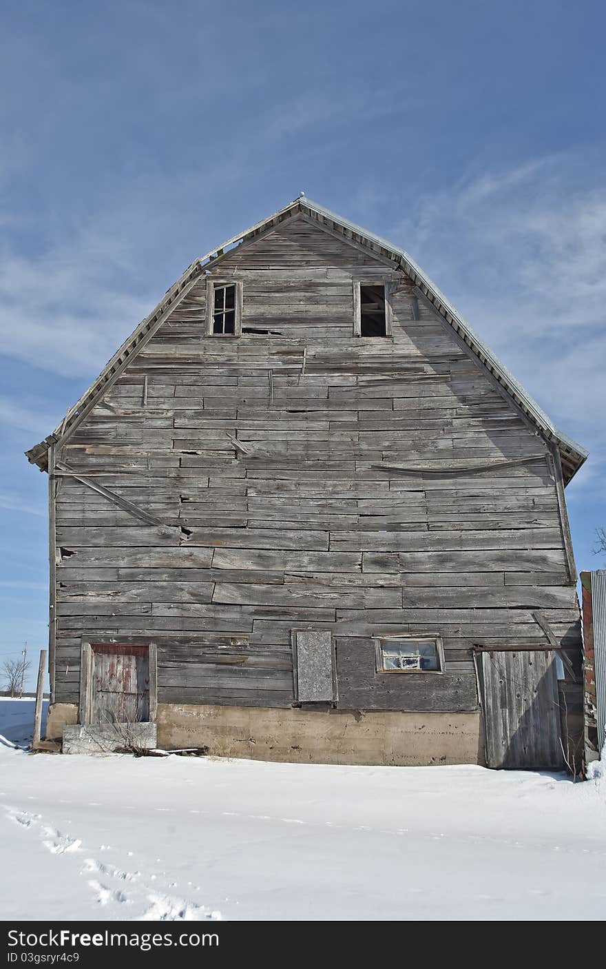 Wooden barn in Wisconsin during winter with snow on the ground and scattered clouds in sky. Wooden barn in Wisconsin during winter with snow on the ground and scattered clouds in sky.