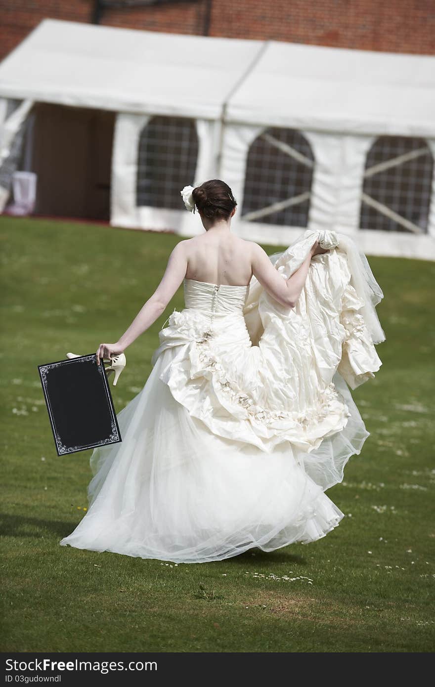 Pretty bride in wedding dress walking away from camera holding a blank board with space for copy. Pretty bride in wedding dress walking away from camera holding a blank board with space for copy