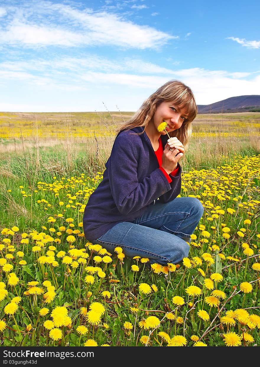 Smiling beautiful girl sitting on a dandelions field with dandelion in her hand. Smiling beautiful girl sitting on a dandelions field with dandelion in her hand