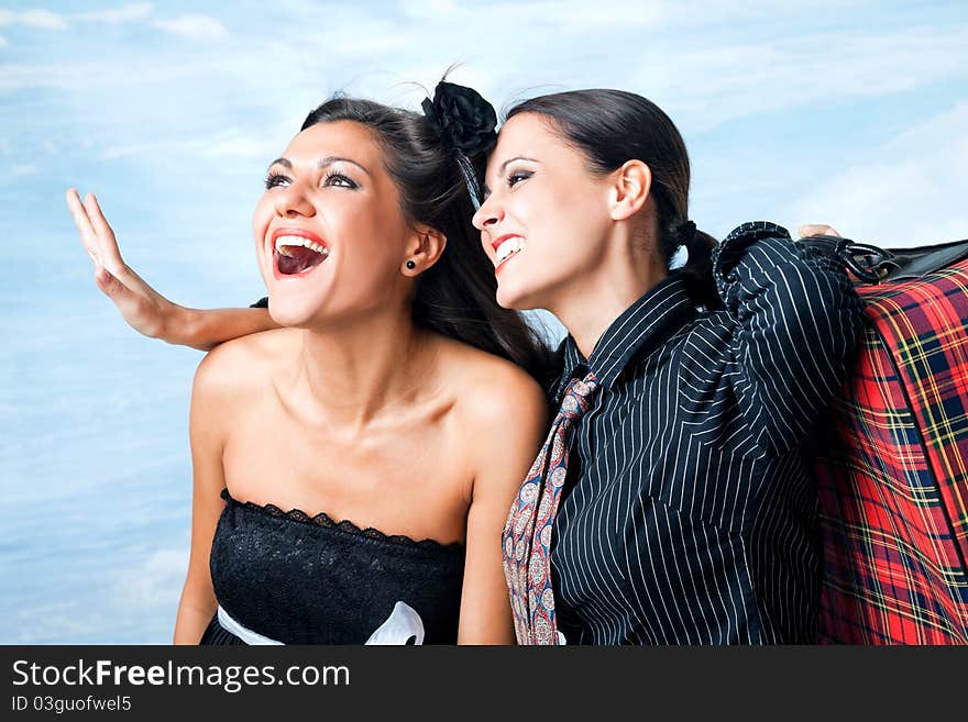 Two beautiful excited females hugging, one carrying suitcase on shoulder. Two beautiful excited females hugging, one carrying suitcase on shoulder