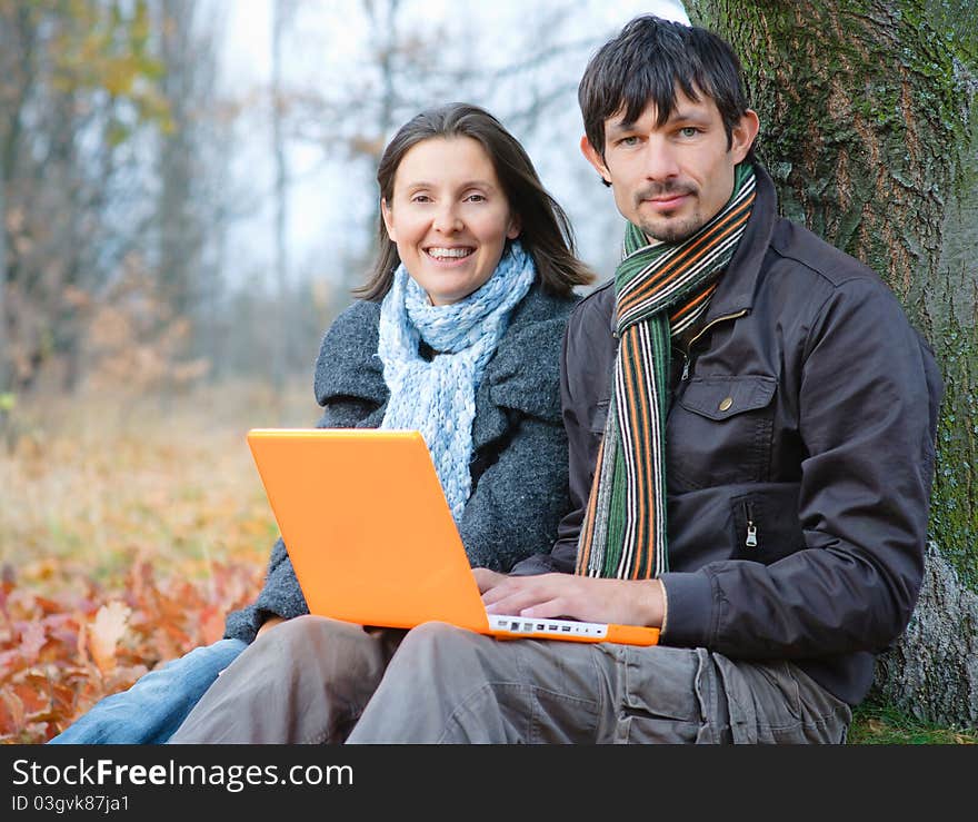 Romantic mature couple sitting with laptop in the autumn park. Romantic mature couple sitting with laptop in the autumn park.