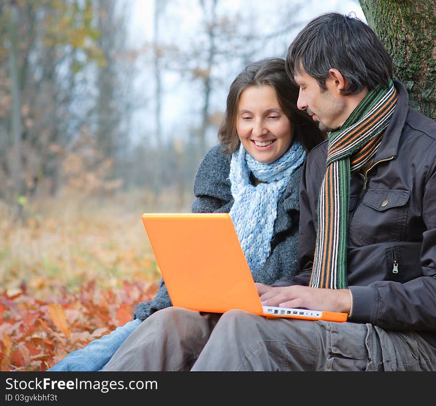 Romantic mature couple sitting with laptop in the autumn park. Romantic mature couple sitting with laptop in the autumn park.