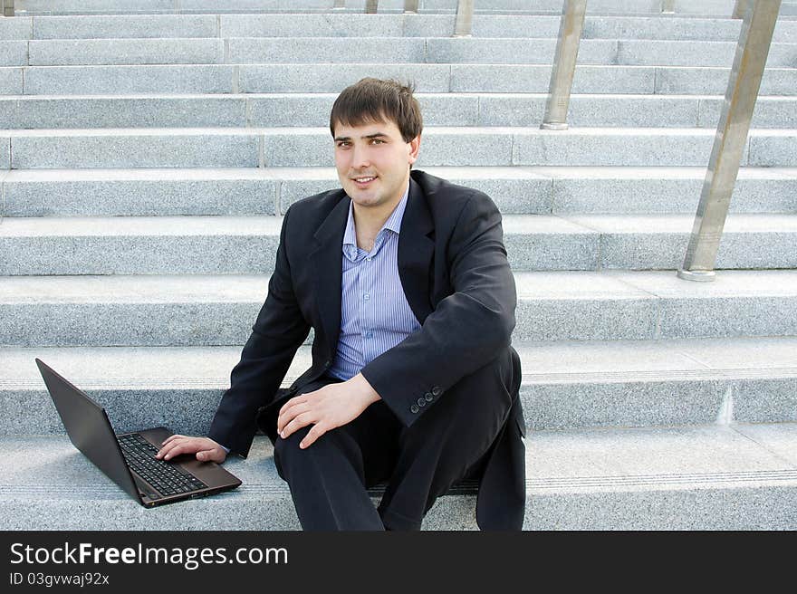 Modern business man outdoors sitting on the stairs of the building with a laptop