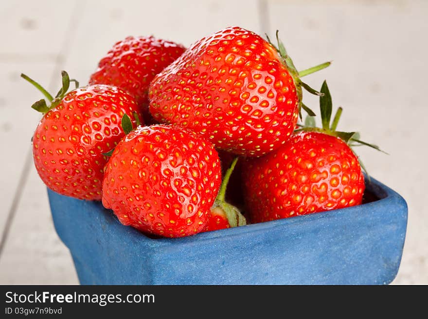 Wet strawberries in a small blue container on a wooden painted table