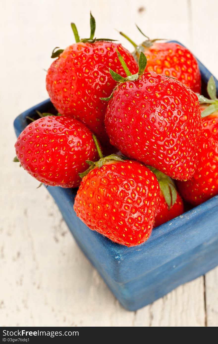 Wet strawberries in a small blue dish on a wooden painted table