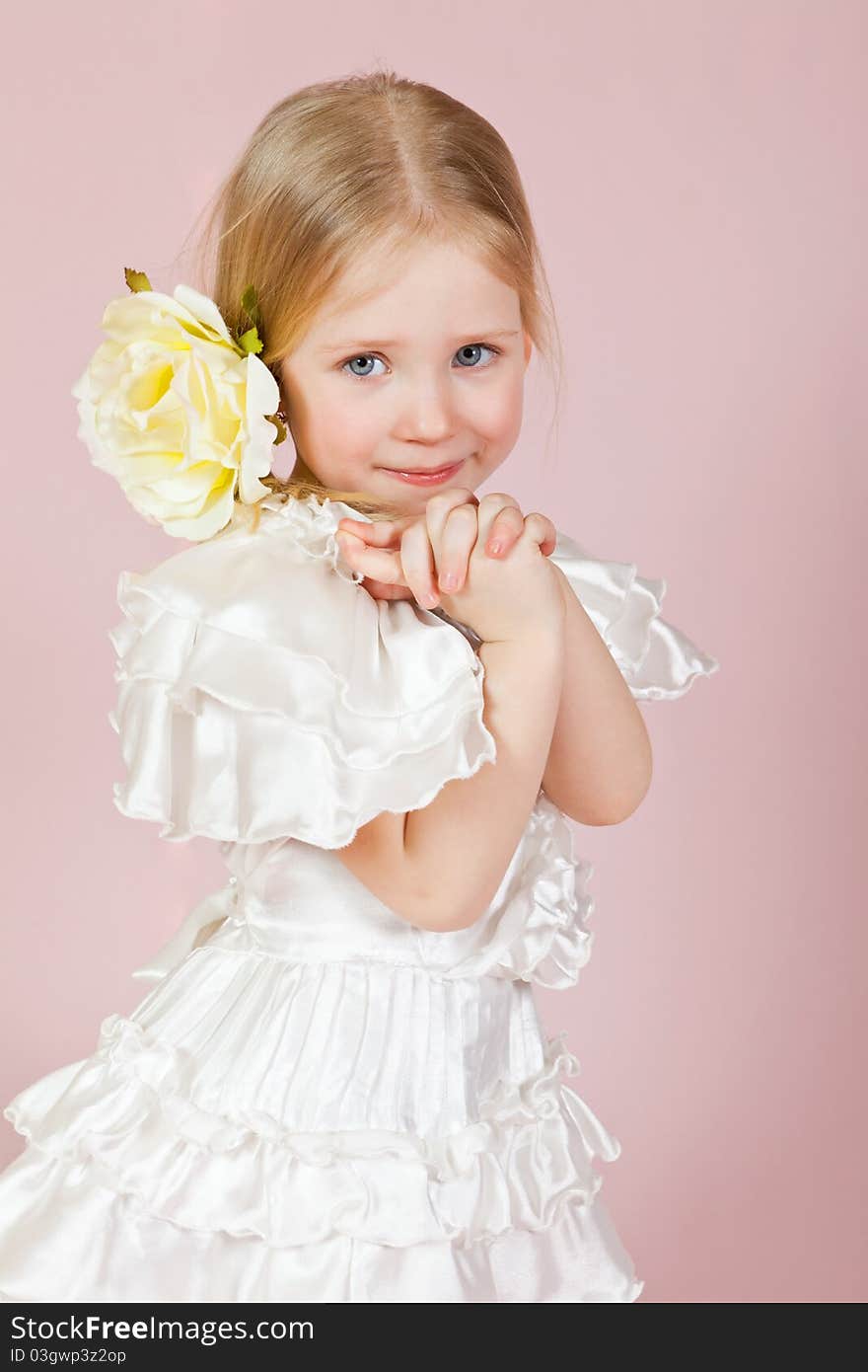 Portrait of the child in a white dress with a flower in hair on a pink background in studio