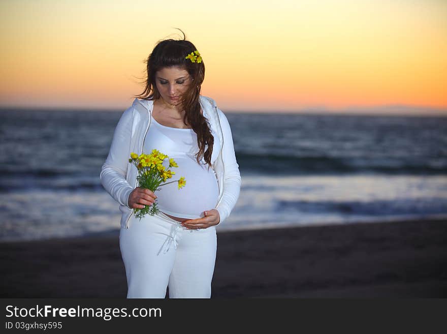 Pregnant woman at the beach during sunset with flowers