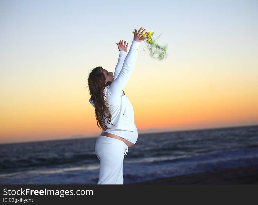 Pregnant woman at the beach during sunset tossing flowers in the air