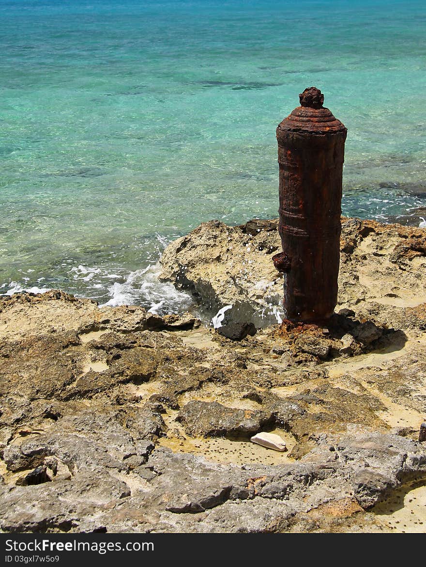 Old rusted bollard on rocky shoreline. Old rusted bollard on rocky shoreline