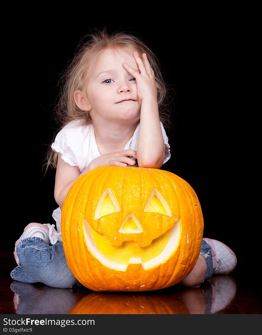 An adorable child is holding her pumpkin trying to make the same face as it. An adorable child is holding her pumpkin trying to make the same face as it.