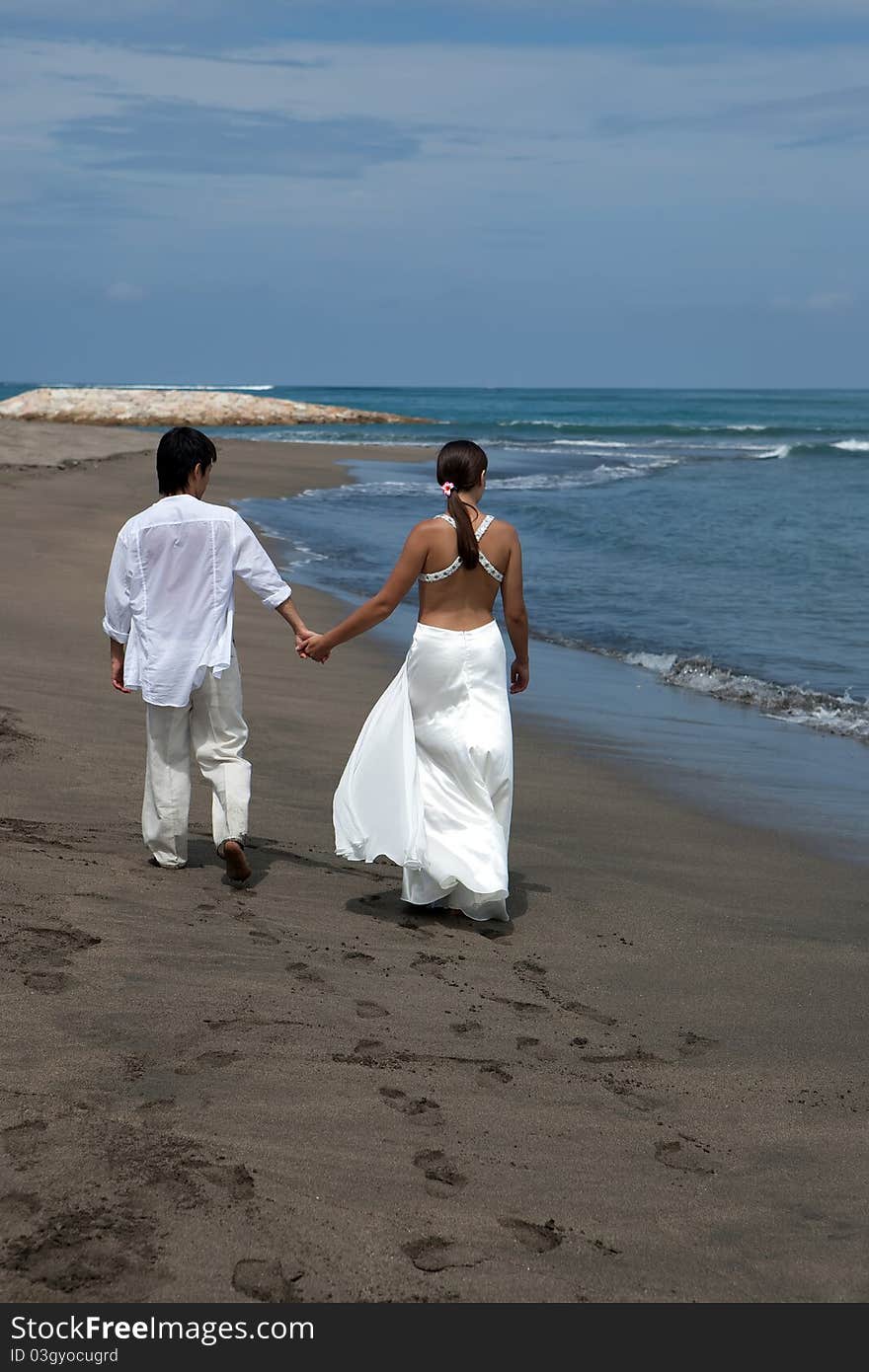 A young couple walk by the water's edge on a beach. A young couple walk by the water's edge on a beach