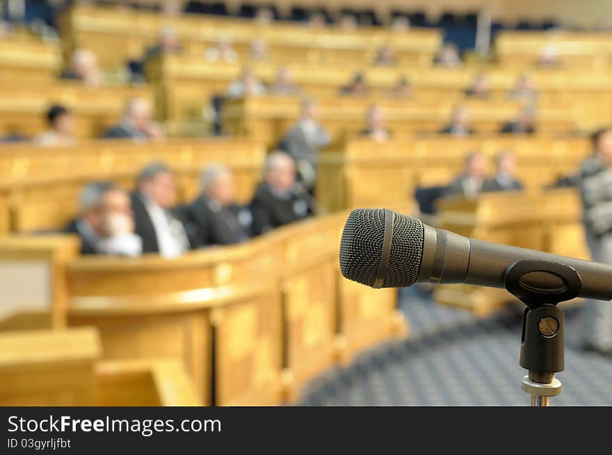Microphone on a stand against the background of unrecognizable people at conference hall. Microphone on a stand against the background of unrecognizable people at conference hall.