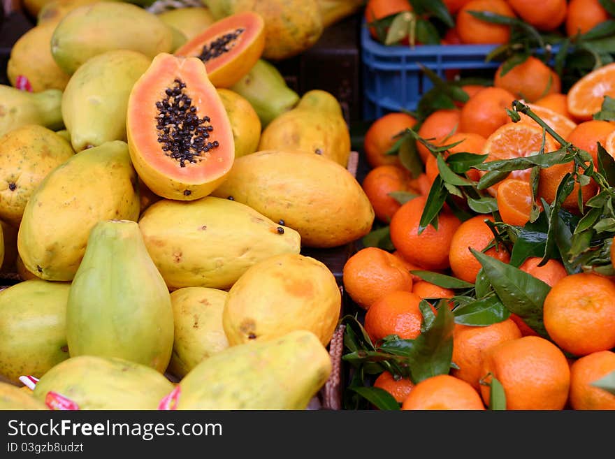 Papaya fruit and mandarin oranges, some of them cut open, on a market stall