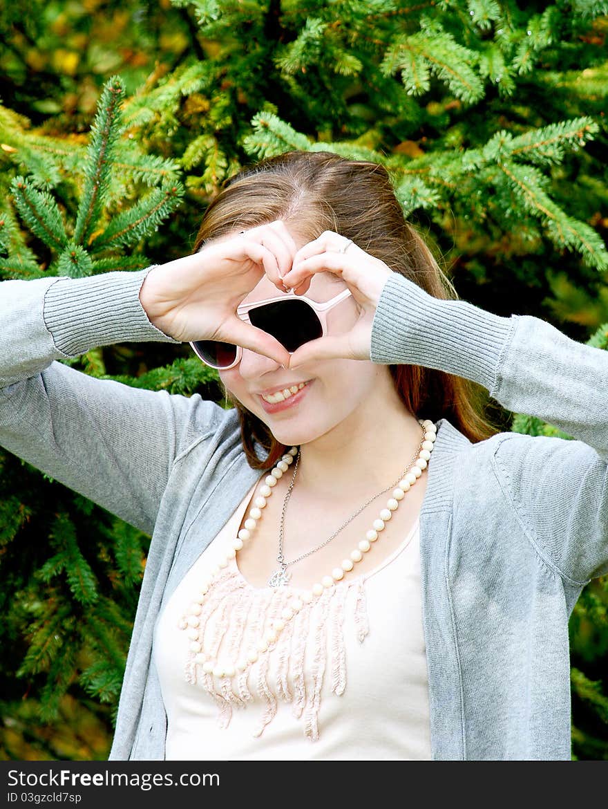 Teen girl outside in front of tree making heart shape around her sunglasses. Teen girl outside in front of tree making heart shape around her sunglasses