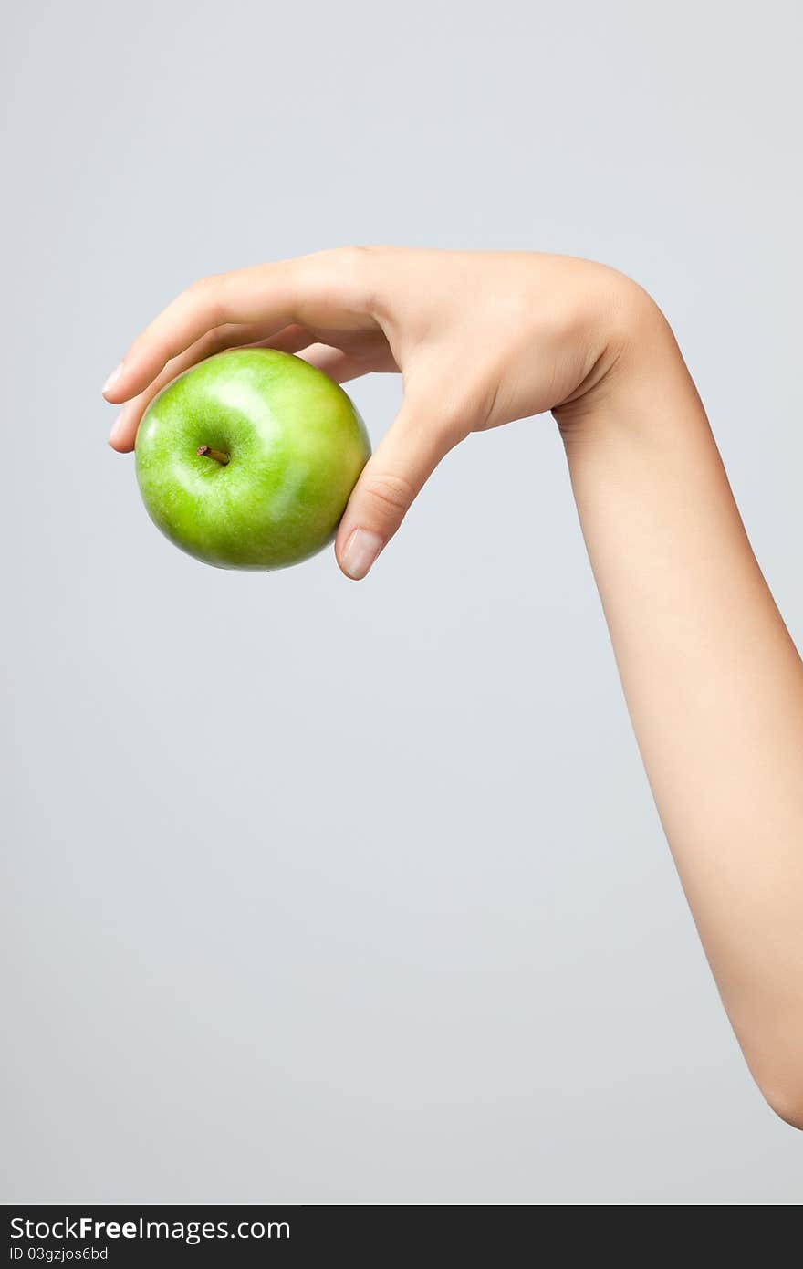 A female Caucasian hand holding a whole green apple on grey studio background. A female Caucasian hand holding a whole green apple on grey studio background.