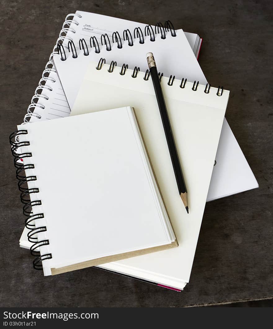 Four Notebook overlapping and black pencil on wood desk