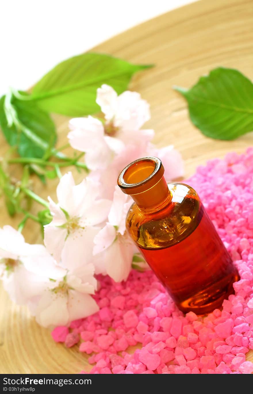 Bottle of essential oil, pink bath salt and flowers