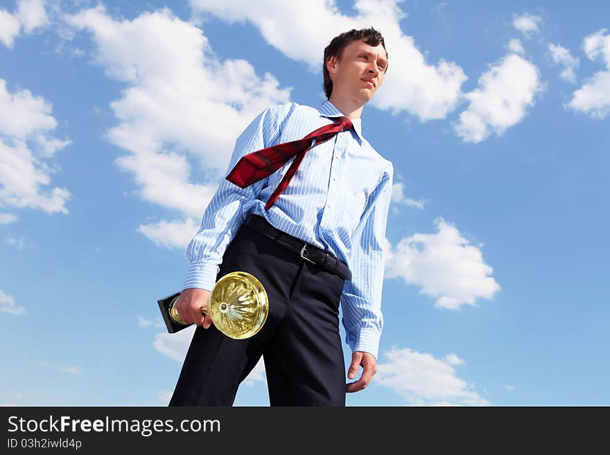 Young businessman in a suit with a golden cup against blue sky. Young businessman in a suit with a golden cup against blue sky