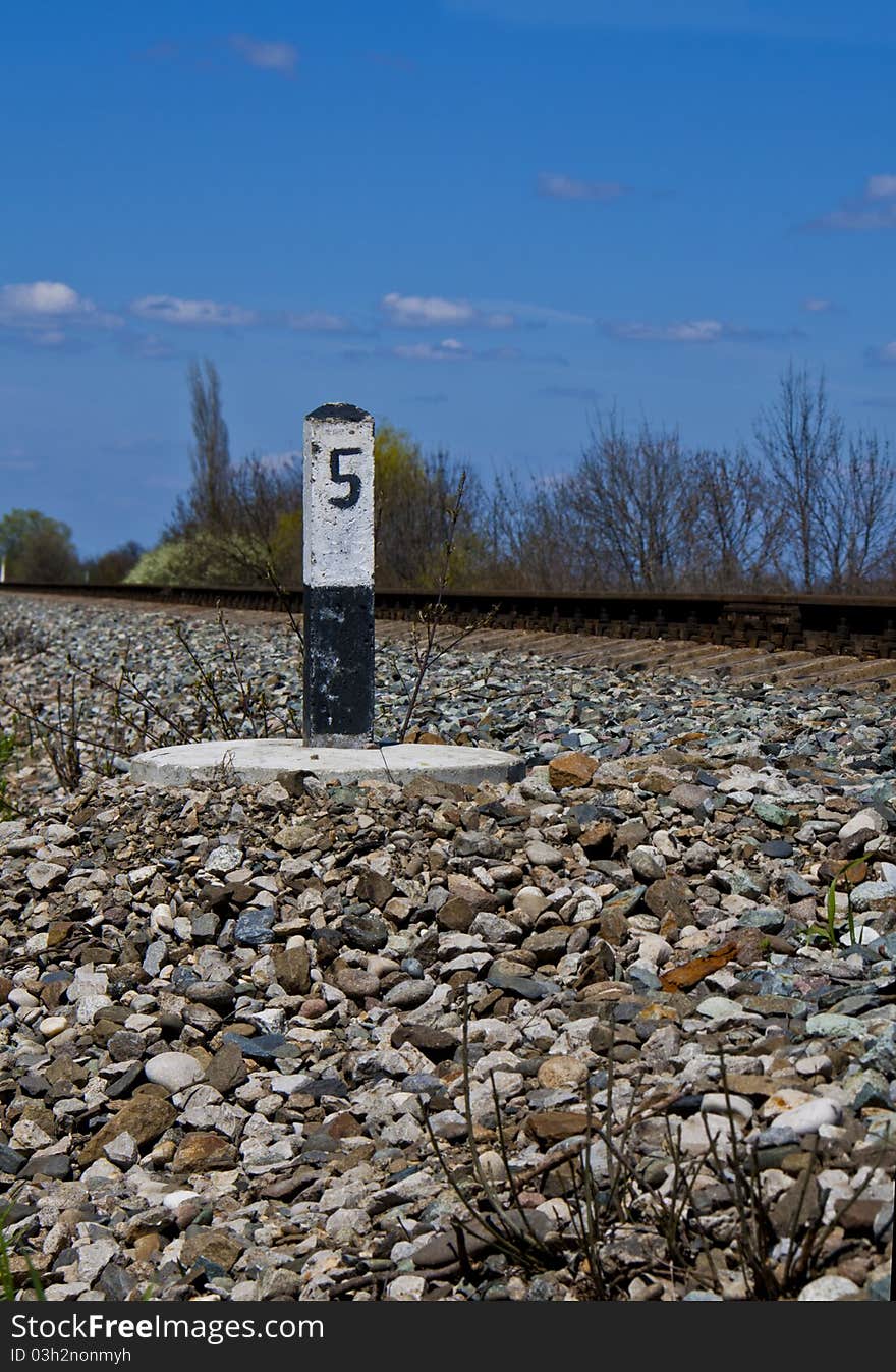 Railway column established on an embankment, against a rail and the blue sky